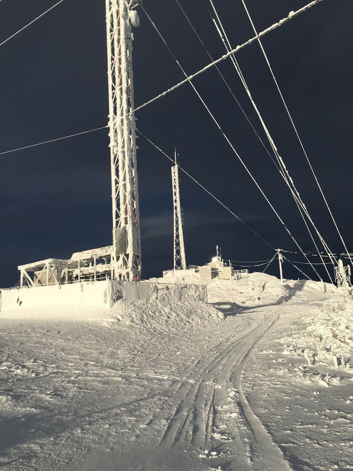 Guyed communications tower lit at night on a snow-covered remote site